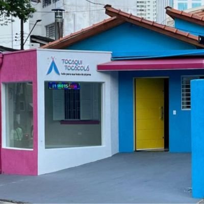 Fachada da Tocaqui Tocacola, com paredes rosa e azul, placa da marca e porta amarela
